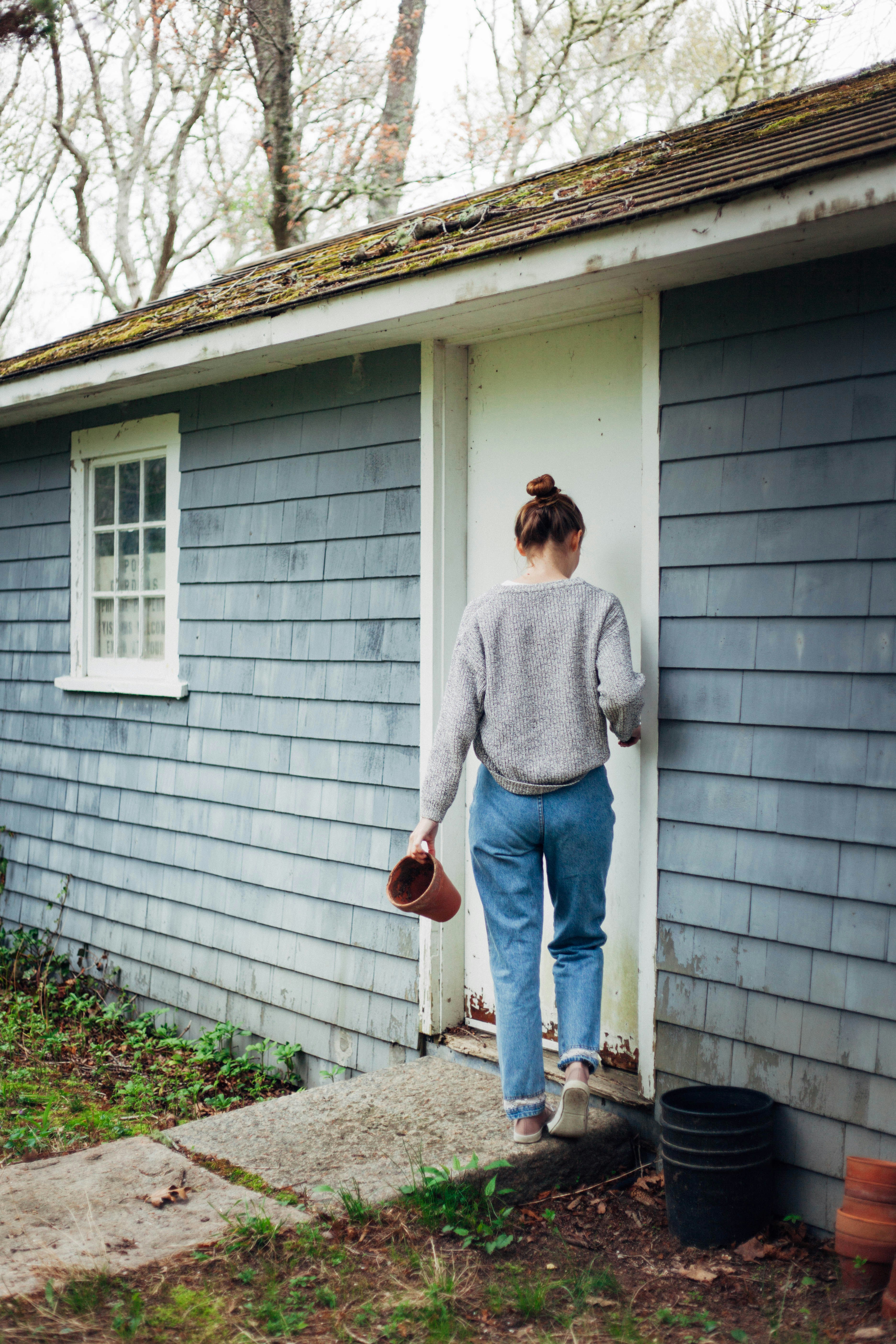 Young woman carrying an empty flower pot enters a gardening shed